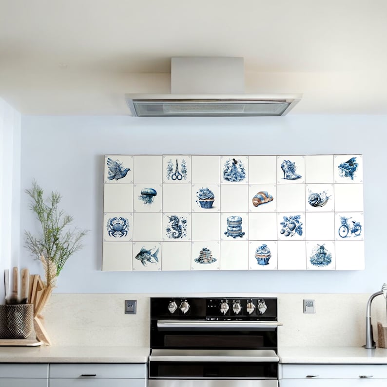May include: A white kitchen with a black range hood and a blue and white tiled backsplash. The backsplash features a variety of images, including a fish, a seashell, a cupcake, and a snail.