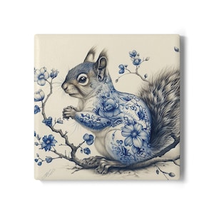 Op de afbeelding: Vierkante keramische tegel met een gedetailleerde illustratie van een eekhoorn met blauwe bloementatoeages. De eekhoorn zit op een tak met blauwe bloemen, tegen een crèmekleurige achtergrond. Het kunstwerk heeft een delicate, artistieke stijl.