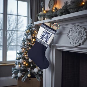 May include: A navy blue Christmas stocking with a white cuff featuring a blue floral design and the letter "A". The stocking is hanging on a fireplace mantel, with a Christmas tree and window in the background.