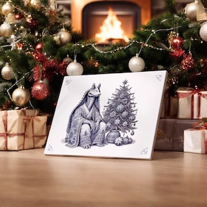 May include: A white ceramic tile featuring a blue and white illustration of a Star Wars character sitting beside a Christmas tree. The character is wearing a robe and has a large head. The Christmas tree is decorated with baubles and a star on top.
