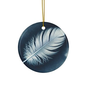 Pode incluir: Uma pena branca sobre um fundo azul escuro. A pena é delicada e parece flutuar no ar. Este é um ornamento de cerâmica.