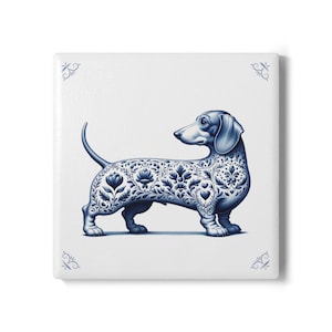Op de afbeelding: Vierkante keramische tegel met een blauw en wit teckelontwerp. De hond is versierd met bloemen- en bladerpatronen. Decoratieve blauwe krullen bevinden zich in elke hoek. De tegel is wit met een glanzende afwerking.