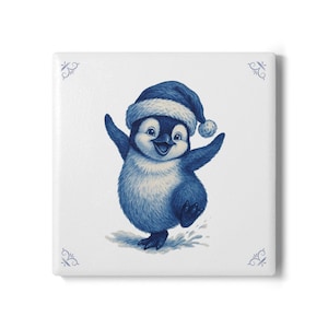 May include: A blue and white ceramic tile featuring a cheerful penguin wearing a Santa hat. The penguin is depicted in a watercolor style, with its arms raised in a joyful pose. Decorative blue flourishes adorn the corners.