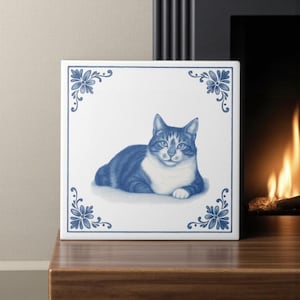 May include: A square ceramic tile with a blue and white illustration of a cat. The cat is depicted lying down with blue stripes and a white chest. Floral corner designs frame the image.