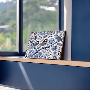 May include: A blue and white ceramic tile featuring a floral design with three birds. The birds are perched on branches and have blue and white feathers.