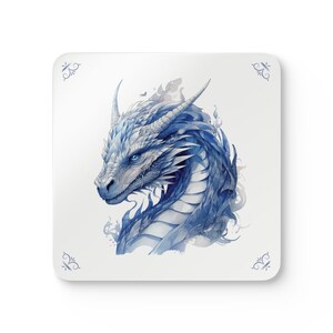 Op de afbeelding: Vierkante onderzetter met een aquarel illustratie van een blauwe drakenkop. De draak heeft gedetailleerde schubben, hoorns en doordringende blauwe ogen. De onderzetter heeft een witte achtergrond met decoratieve hoekaccenten.