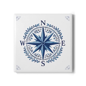 Puede incluir: Azulejo blanco cuadrado con un diseño de rosa de los vientos azul. La rosa de los vientos está rodeada por una corona circular de hojas azules y las direcciones cardinales están etiquetadas N, E, S y O. Acentos florales azules decorativos en cada esquina.