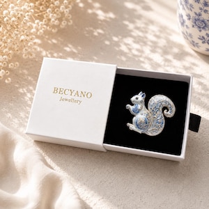 May include: A silver-toned squirrel brooch with intricate blue and white enamel detailing, featuring delicate floral patterns. The brooch is presented inside a white rectangular jewelry box with the text BECYANO Jewellery printed in gold.