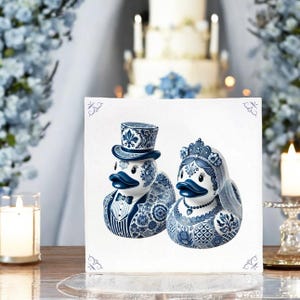 May include: A pair of blue and white ceramic duck figurines dressed as a bride and groom. The groom is wearing a top hat and bow tie, while the bride is wearing a crown and veil. The figurines are on a white background.