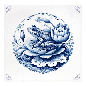 May include: A blue and white ceramic tile with a detailed illustration of a frog sitting on a lily pad. The tile is decorated with a floral border.