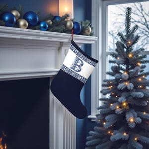 Op de afbeelding: Een marineblauwe kerstsok met een wit paneel met een bloemmotief en de letter "B". De sok hangt voor een open haard, met een versierde schoorsteenmantel en een kerstboom op de achtergrond.