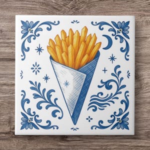 May include: Square ceramic tile with a watercolour illustration of a cone of golden french fries. The fries are in a blue and white paper cone, surrounded by blue floral and star designs. The tile is on a wooden surface.