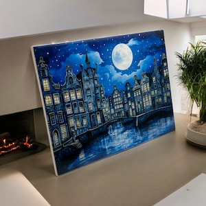 Puede incluir: Una pintura de un horizonte urbano de noche con una luna llena en el cielo. Los edificios son azules y blancos y tienen ventanas. El agua del canal es azul oscuro y refleja las luces de la ciudad. El cielo es azul oscuro con estrellas blancas.