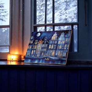 Può includere: Un dipinto che rappresenta una scena notturna innevata con una fila di case con finestre illuminate. Le case sono dipinte in tonalità di blu e giallo, e il cielo è di un blu scuro con luna piena e stelle. Una piccola barca si trova nell'acqua di fronte alle case.