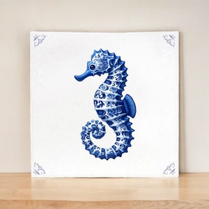 Könnte beinhalten: Eine quadratische, weiße Leinwand zeigt eine detaillierte blaue Seepferdchen-Illustration. Das Seepferdchen ist mit aufwendigen floralen Mustern verziert, und die Ecken der Leinwand haben kleine blaue dekorative Elemente. Das Seepferdchen ist der Mittelpunkt des Kunstwerks.