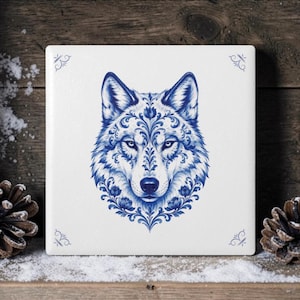 Può includere: Una piastrella quadrata in ceramica bianca con un'illustrazione blu centrata di una testa di lupo. Il lupo è decorato con intricati motivi floreali e a volute in uno stile a inchiostro blu intenso. Sono presenti piccoli accenti decorativi blu.