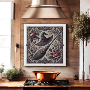 Könnte beinhalten: Ein quadratischer Leinwanddruck mit einem schwarzen Hexenhut und einem Besen, umgeben von floralen Designs in den Farben Rosa, Grün und Braun.