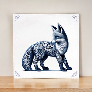 Könnte beinhalten: Quadratische, weiße dekorative Fliese mit einer blauen Fuchsdarstellung. Der Fuchs ist mit floralen Mustern verziert und steht vor einem weißen Hintergrund. Dekorative blaue Eckakzente vervollständigen das Design. Die Fliese wird auf einer Holzoberfläche präsentiert.