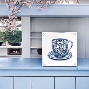 May include: A blue and white ceramic teacup and saucer with a decorative floral pattern and the text "I LOVE MAMA" in the centre. The teacup and saucer are on a white background.