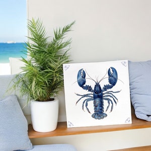 Könnte beinhalten: Eine Illustration eines blauen Hummers auf einer weißen Fliese mit blauem Rand. Der Hummer ist mit erhobenen Scheren nach vorne gerichtet. Die Fliese ist vor einem weißen Hintergrund platziert.