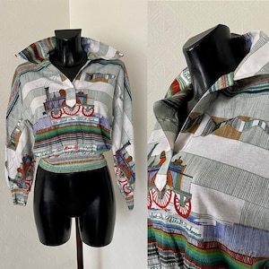 Könnte beinhalten: Ein weißes, kurzes, langärmeliges Hemd mit einem bunten Druck einer Lokomotive. Das Hemd hat einen spitzen Kragen und einen Knopfverschluss. Der Druck enthält den Text "The Rocket 1432.R.Stephenson".