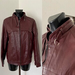 May include: A burgundy leather jacket with a zipper closure and a ring detail on the collar.