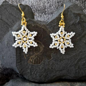 Op de afbeelding: Een paar witte sneeuwvlok oorbellen met gouden accenten. De oorbellen zijn gemaakt van kleine kralen en hebben een delicaat, ingewikkeld ontwerp.