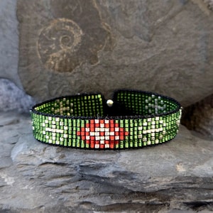 Könnte beinhalten: Ein grünes und rotes Perlenarmband mit einem roten Herzdesign. Das Armband besteht aus kleinen, quadratischen Perlen und ist auf einer schwarzen Schnur aufgefädelt.