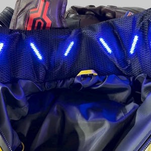 May include: A bright yellow and black jacket featuring a high collar lined with black mesh fabric. The collar contains a series of small, bright blue LED lights arranged in a row. The jacket has a dark interior lining and a front zipper closure.
