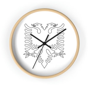 Könnte beinhalten: Eine weiße Uhr mit einer schwarzen Umrandung des albanischen Doppelkopfadels auf dem Zifferblatt. Die Uhr hat schwarze Zeiger und einen Holzrahmen.