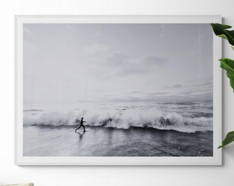 Puede incluir: Una fotografía en blanco y negro de una persona corriendo hacia las olas del océano. Las olas rompen en la costa y el cielo está nublado.