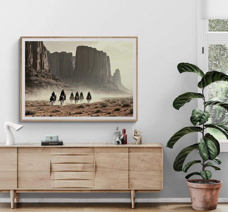 May include: A framed print of a landscape scene with five figures on horseback riding through a desert canyon. The figures are silhouetted against the bright sky. The canyon walls are a reddish-brown colour.