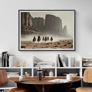 May include: A framed photograph of a group of people riding horses through a desert landscape. The horses are silhouetted against a hazy, dusty background. The landscape is dominated by tall, red rock formations.