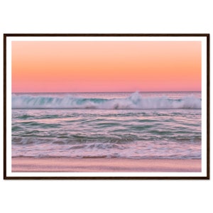 May include: A pink and orange sunset over a turquoise ocean with white foamy waves crashing on the sandy beach.
