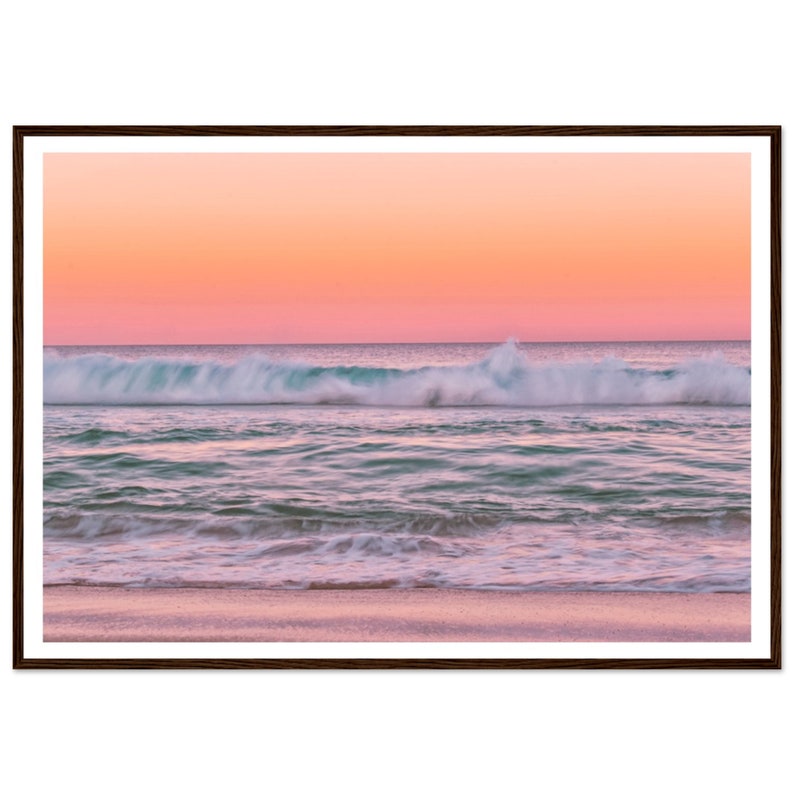 May include: A pink and orange sunset over a turquoise ocean with white foamy waves crashing on the sandy beach.