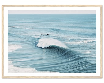 Puede incluir: Una fotografía de una gran ola rompiendo en el océano. La ola es de color azul claro y tiene una cresta blanca. Hay varios surfistas en el agua, montando la ola.