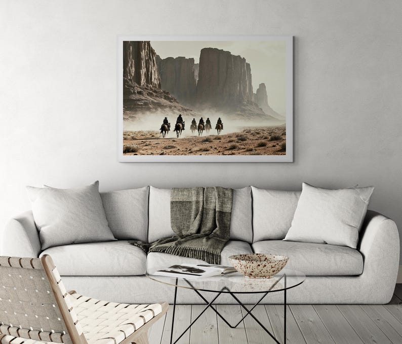 May include: A framed photograph of a group of people riding horses through a desert landscape. The photograph is in a white frame and features a muted colour palette of browns, tans, and greys. The horses are moving in a line, and the riders are wearing dark clothing.