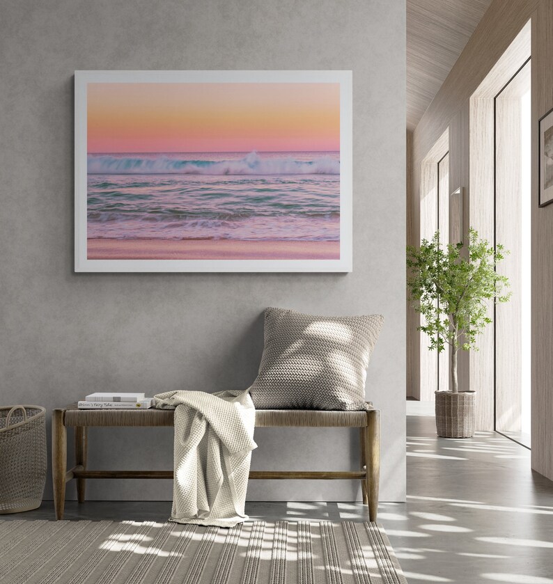 May include: A framed photograph of a pink and orange sunset over a calm ocean with a single wave breaking in the foreground.