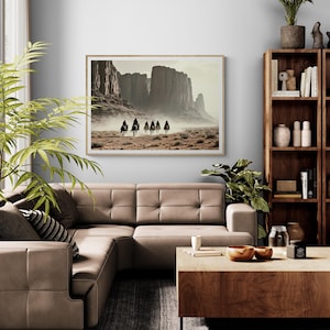 May include: A framed photograph of a group of people riding horses through a desert landscape. The photograph is in a light wood frame and is hanging on a wall in a living room.