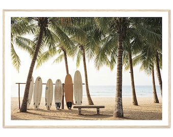 May include: A framed print featuring a beach scene with palm trees and surfboards. Six surfboards lean against a wooden rack on the sandy beach. A concrete bench sits in front of the surfboards. The ocean is visible in the background.