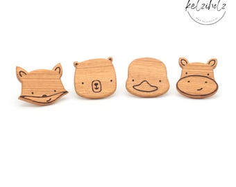 May include: Four wooden animal-shaped buttons featuring engraved faces of a fox, a bear, a duck, and a hippo. Each piece displays a natural light brown wood grain with dark brown laser-etched details. The logo kelziholz is visible in the corner.