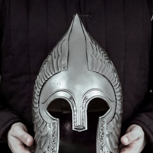 May include: A silver helmet with a pointed top and decorative details. The helmet has a face mask with eye holes and a chin strap.