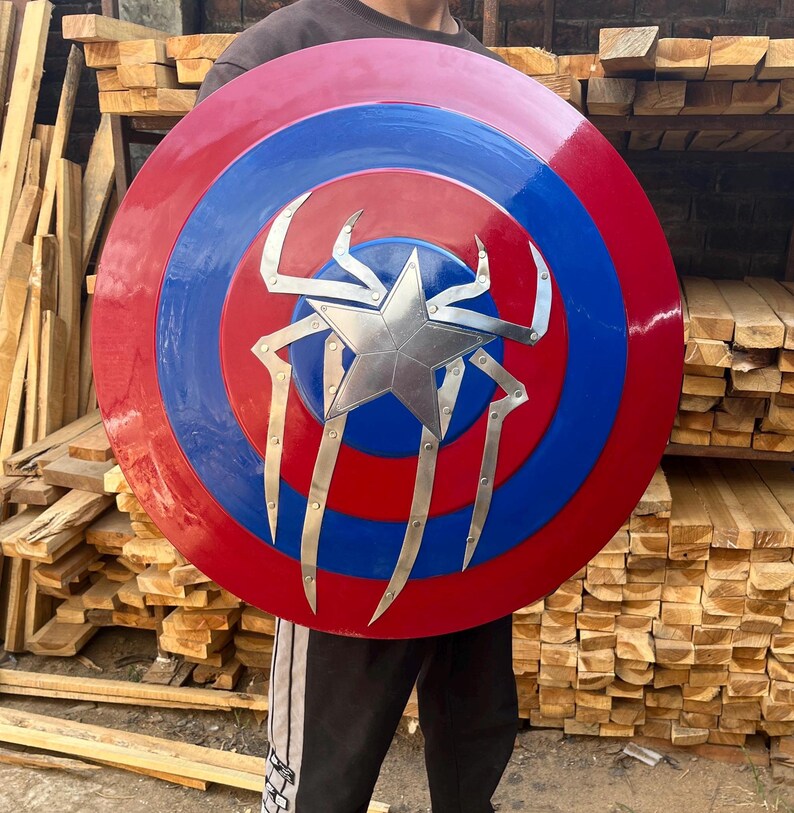 Puede incluir: Un escudo de Capit&aacute;n Am&eacute;rica rojo, blanco y azul con un dise&ntilde;o de ara&ntilde;a plateado en el centro.