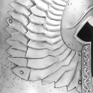May include: A silver helmet with a winged design. The helmet has a textured surface and a pointed top.