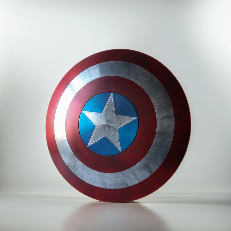 May include: A red, white, and blue Captain America shield with a silver star in the center. The shield is round and has a raised edge.
