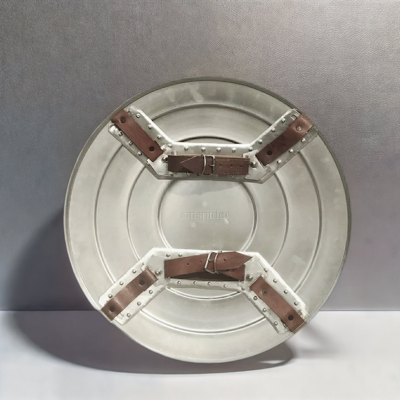 May include: The back of a silver Captain America shield with brown leather straps and buckles. The shield has the word "cospider" printed on it.