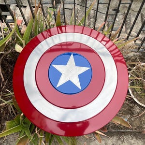 May include: A red, white, and blue Captain America shield with a five-pointed star in the center. The shield is made of metal and has a shiny finish.