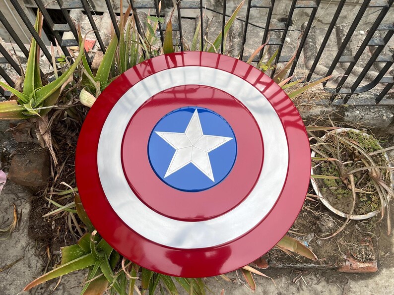 May include: A red, white, and blue Captain America shield with a five-pointed star in the center. The shield is made of metal and has a shiny finish.