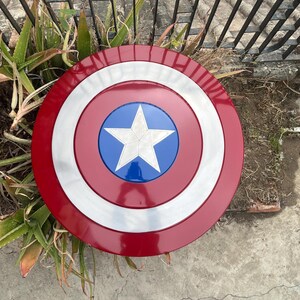 May include: A red, white, and blue Captain America shield with a five-pointed star in the center. The shield is made of metal and has a shiny finish.