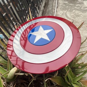 May include: A red, white, and blue Captain America shield with a five-pointed star in the center. The shield is made of metal and has a shiny finish.